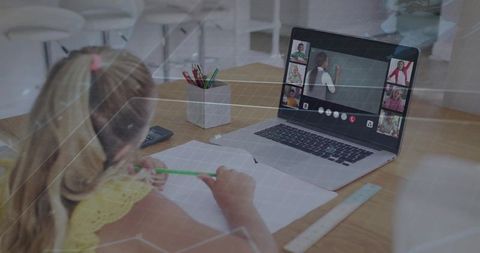 Young child writing while attending interactive online class on laptop at home study desk