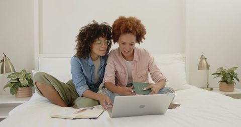 Middle-aged women planning trip on laptop in bright bedroom with plants and notes