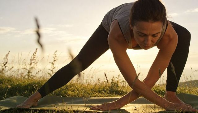 Sunset meadow yoga practicing woman holding forward bend on mat barefoot