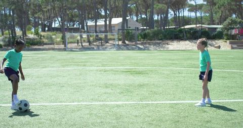 Youth girls practicing soccer dribbling on sunlit artificial turf during outdoor training