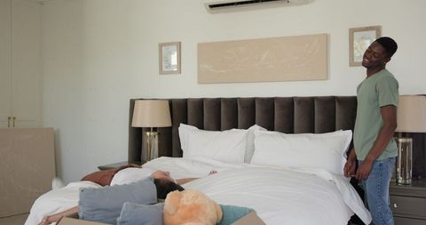 Young Couple Laughing While Making Bed in Cozy Bedroom