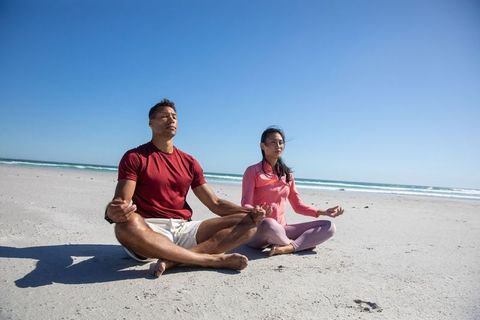 Diverse Couple Meditating on Oceanfront Beach Under Blue Sky