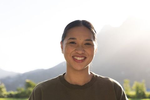 Sunlit smiling asian woman in olive crewneck backlit by mountain valley morning light