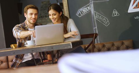 Two Young People Collaborating on Laptop at Cafe