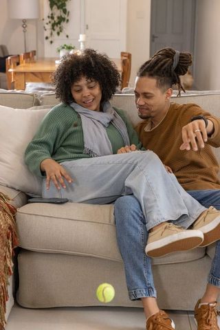 African american couple sitting on sofa sharing phone while ball bouncing in cozy room