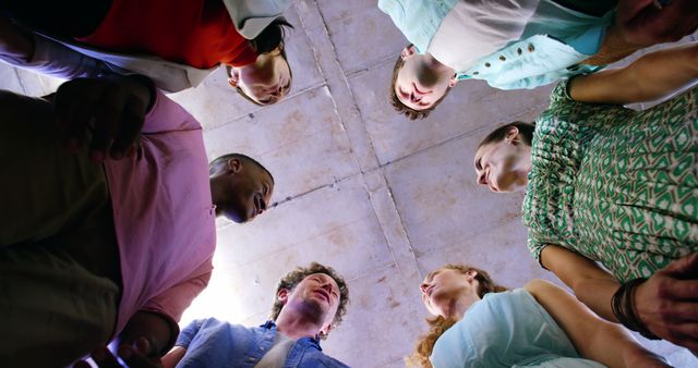Various individuals of different ethnic backgrounds standing closely in a circle, collectively looking upwards. Useful for concepts related to teamwork, collaboration, unity, and diversity in workplace or community settings.