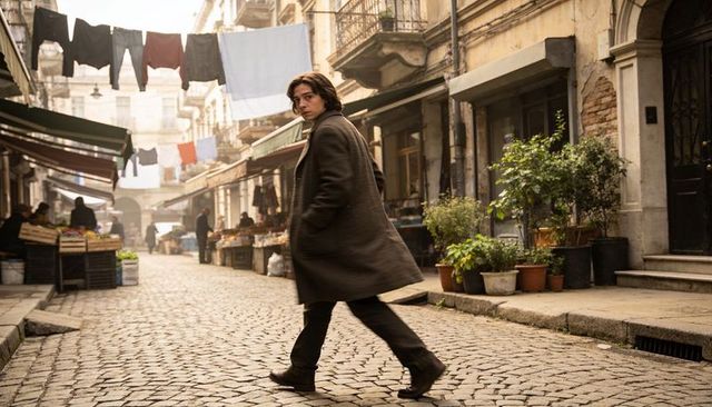 Young man walking through historic cobblestone market street, turning back with glance