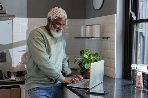 Senior african american man working on laptop at kitchen counter, daylight lifestyle