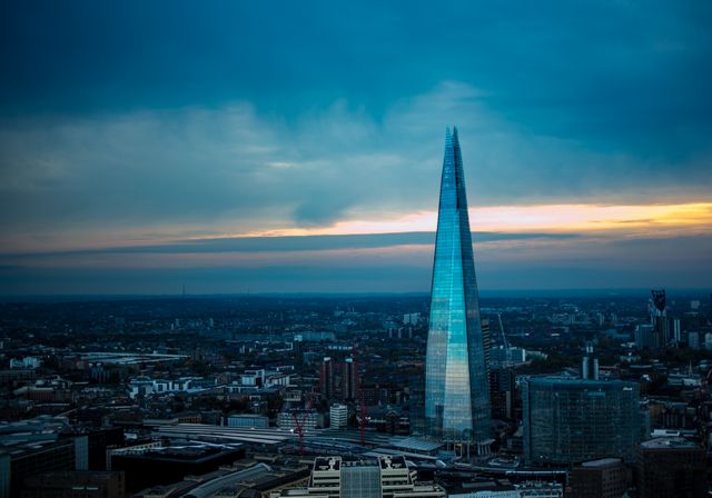 Silhouette of The Shard dominating the urban landscape during sunset. Perfect for travel and tourism campaigns promoting London, business-related uses showcasing modern architecture and iconic skylines, as well as presentations highlighting urban beauty and dynamic evening cityscapes.