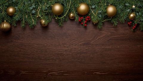 Gilded christmas garland decorating dark wood tabletop with evergreen, gold baubles, berries