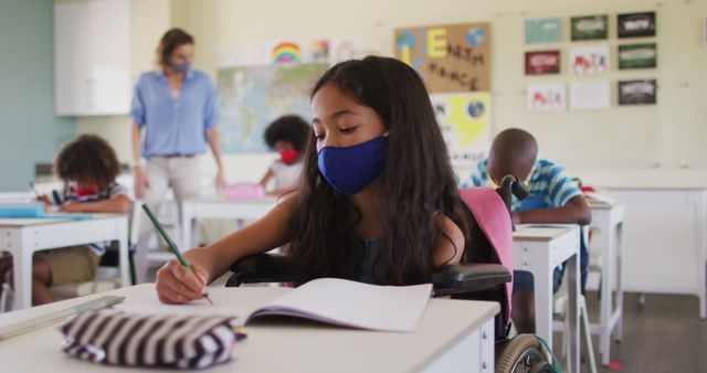 Young Student in Mask Writing in Classroom with Teacher Assisting in Background - Download Free Stock Images Pikwizard.com