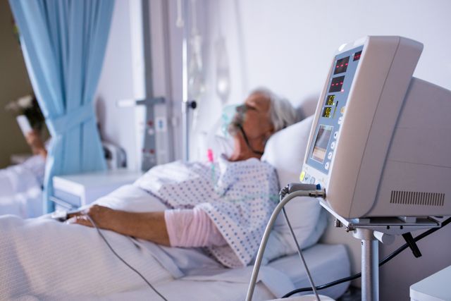 Vital signs monitor with senior patient relaxing in the background at hospital