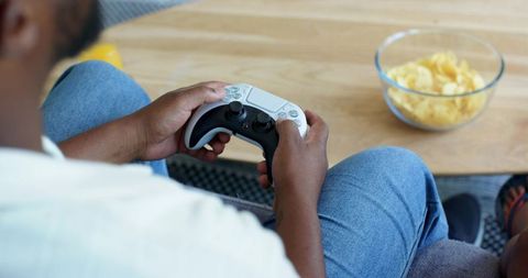 African american friends playing video game with white controller on couch with chips