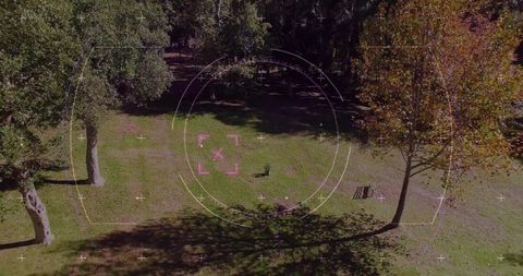 Aerial hud target overlay over park clearing with wooden bench, autumn trees, sunlit lawn