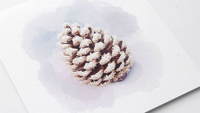Resting snow-dusted pine cone on lavender watercolor paper, minimalist winter still life