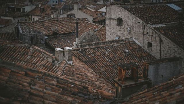Weathered Terracotta Rooftops Showcasing Chimneys, Rusted Vent and Arched Window