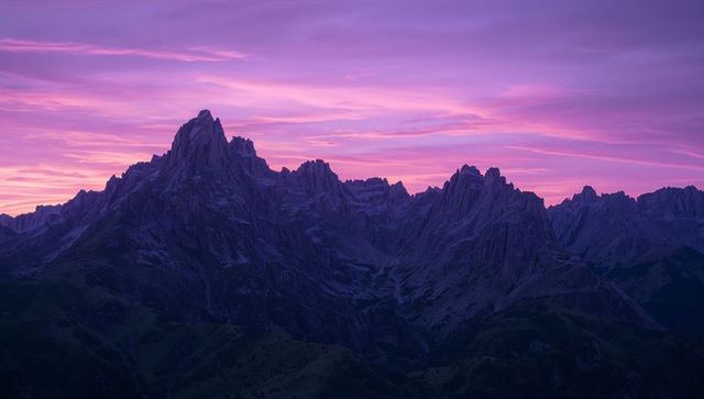 Violet twilight casting jagged alpine ridge silhouette under striking pink and purple sky