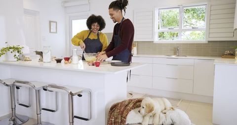 Couple mixing batter at modern white kitchen island with puppy resting on rug