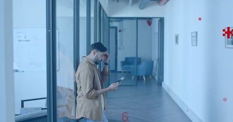 Man walking in glass office corridor holding tablet