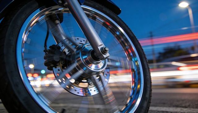 Spinning motorcycle wheel with chrome rim and light trails at urban dusk motion blur close-up
