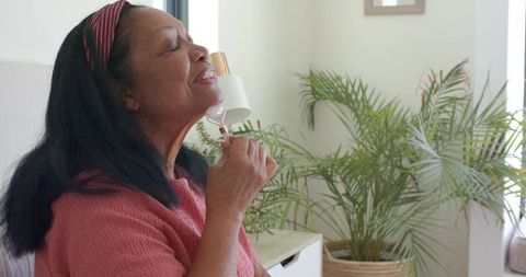 Senior african american woman using rose quartz facial roller for daily skincare routine