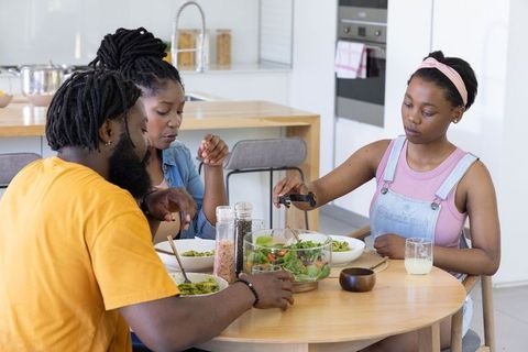 African american family sharing healthy salad at round table in bright modern kitchen