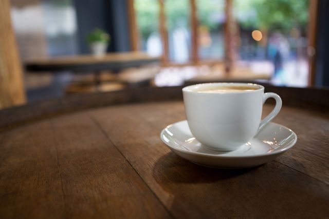 Cup of coffee on wooden table in cozy cafe. Ideal for use in articles or advertisements related to coffee shops, relaxation, morning routines, or cozy interiors. Perfect for promoting cafes, coffee brands, or lifestyle blogs.