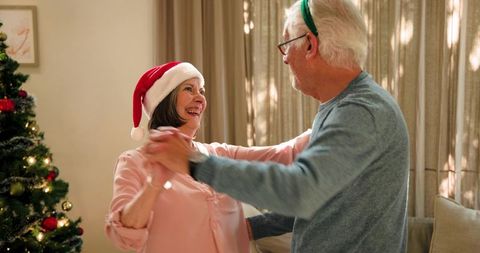 Senior Couple Dancing Joyfully by Christmas Tree with Festive Hats