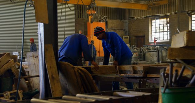 Two factory workers wearing blue jackets working together with machinery and tools in an industrial workshop. Suitable for topics related to manufacturing, teamwork, engineering, industrial work environment, and craftsmanship.