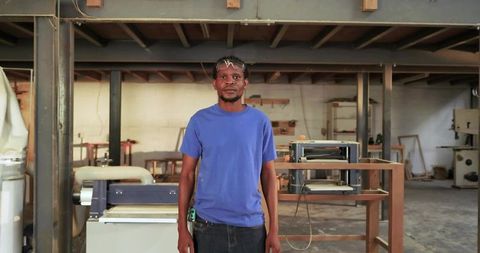Carpenter standing in woodworking workshop wearing safety glasses and tape measure
