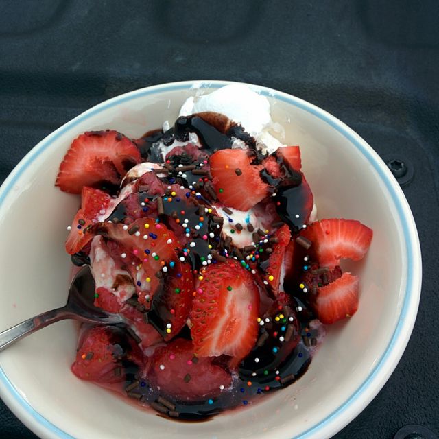 Closeup of a bowl filled with vanilla ice cream, fresh strawberries, and chocolate sauce, with colorful sprinkles on top. Perfect for illustrating dessert recipes, food blogs, menus, or advertisements for ice cream parlors.
