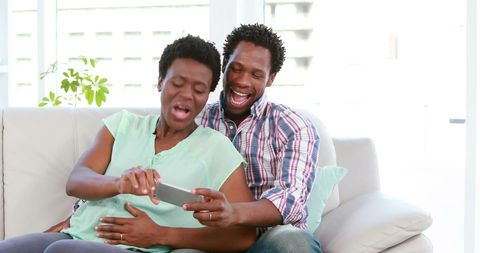 Laughing Couple Sharing Fun Moment on Couch with Smartphone