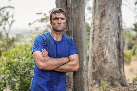 Man Leaning on Wooden Post in Rural Bushland Wearing Sweat-stained Blue T-shirt
