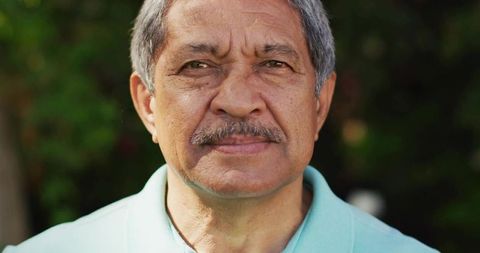 Senior Hispanic man facing camera wearing turquoise polo outdoors showing facial texture