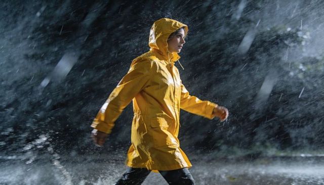 Woman walking wearing yellow raincoat through rainy night, backlit rain and puddles