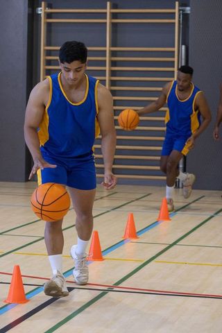 Basketball players dribbling through cones in gym for practice