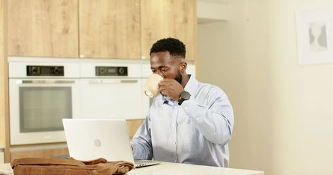 African American man sipping coffee while working on laptop at modern kitchen island