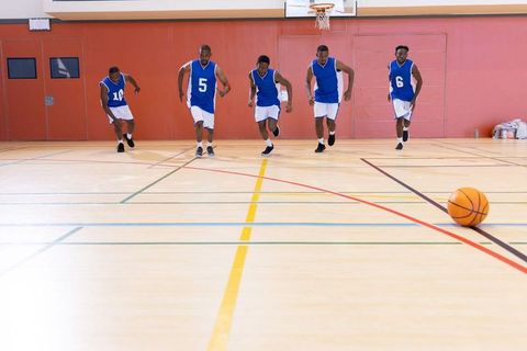 African american basketball players sprinting across gym court during intense conditioning