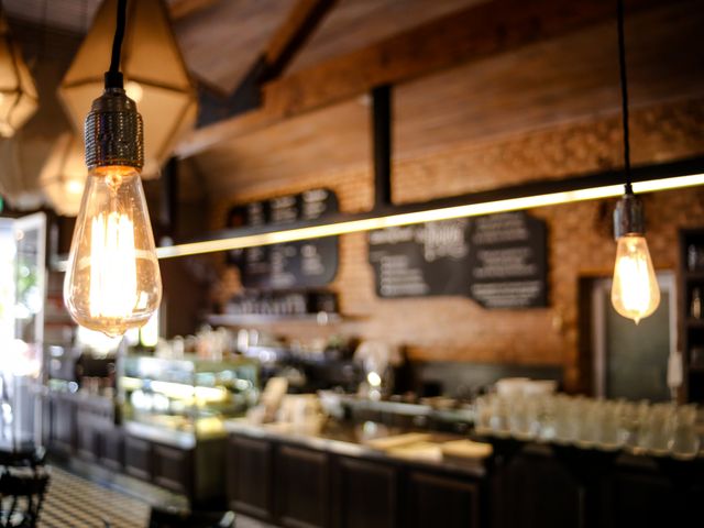 This image showcases a contemporary café interior with warm lighting from Edison bulbs. The ambiance is cozy and inviting, featuring wooden decor and menu boards in the background. Useful for articles or advertisements related to cafés, interior design, or modern restaurant trends.