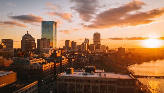Glowing boston skyline reflecting golden sunset over charles river waterfront at dusk