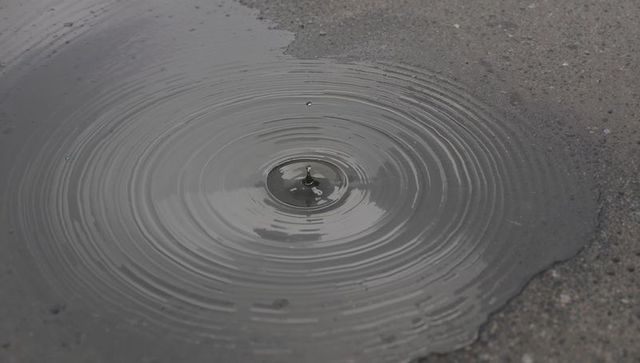 Concentric ripples forming on wet asphalt with central droplet splash