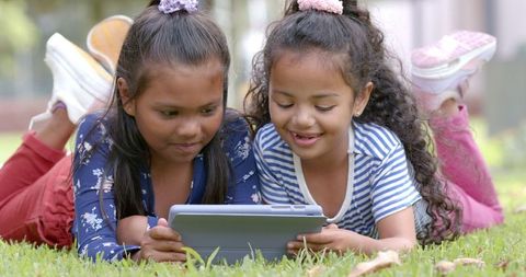 Girls Using Tablet Together Outdoors on Grass