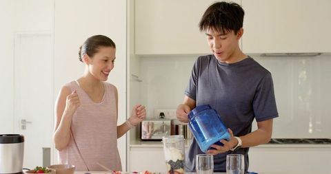 Young couple preparing healthy fruit yogurt smoothie together in bright modern kitchen