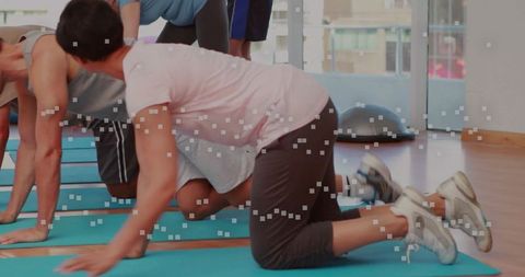 Mid adult woman kneeling on mat following coach cues during group core mobility class