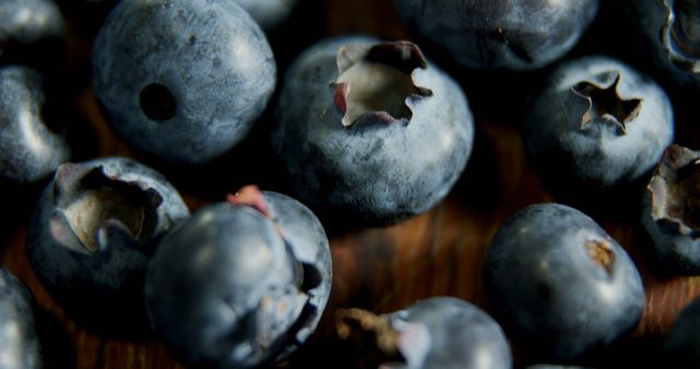 Macro shot of ripe blueberries on wooden surface showcasing details and texture. Perfect for use in health food promotions, organic product advertisements, or culinary blogs focusing on nutritious ingredients.
