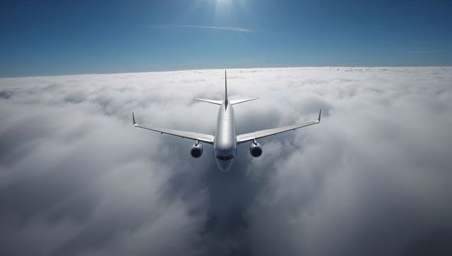 Flying white twinjet approaching through cloud deck under bright sun and clear blue sky