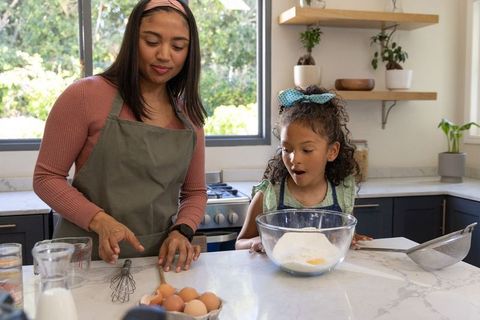 Mother and daughter baking together on marble kitchen island, mixing bowl, family bonding