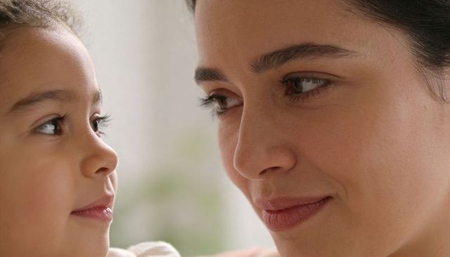 Mother and daughter sharing tender eye contact near window creating intimate maternal bond