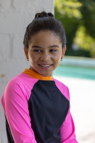 Smiling teen in pink rash guard by backyard pool enjoying sunny summer day