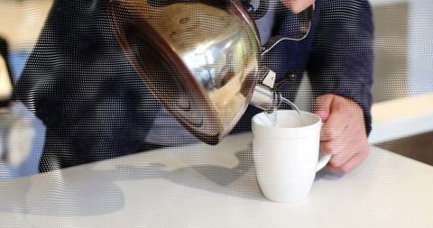 Man Pouring Beverage from Kettle into Mug at Modern Cafe Counter